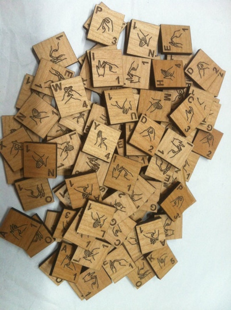 May include: A set of wooden tiles with different hand signs and letters engraved on them. The tiles are scattered on a white surface.