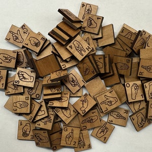 May include: A pile of small, square wooden tiles, each engraved with hand gestures and numbers. The tiles are various shades of brown with black line art. The image shows a variety of hand signs, including letters and numbers, likely for educational purposes.