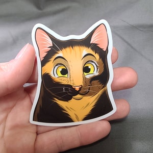 May include: A sticker of a cartoon cat with black, orange, and white fur. The cat has large, yellow eyes and a friendly expression.