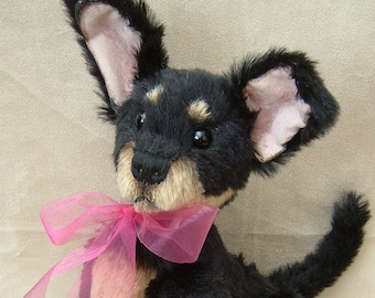 May include: A black and tan plush toy dog with pink ribbon around its neck. The dog is sitting with its head tilted and looking up.