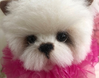 Puede incluir: Un oso de peluche blanco y esponjoso con orejas marrones y ojos negros que lleva un collar de volantes rosa.