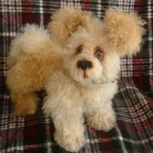May include: A light tan, fluffy plush dog toy. The dog has large, floppy ears, a black nose, and brown eyes. It is posed in a standing position, with its paws visible. The soft toy is handmade.