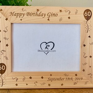 May include: A wooden picture frame with a light brown finish. The frame has a laser-engraved design of confetti, stars, and a balloon with the number 60. The text "Happy Birthday Gino" and "September 18th, 2019" are also engraved on the frame.