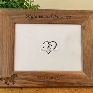 May include: A personalized walnut wood picture frame with the names "Malaree and Presence" engraved on the top. The frame also has a heart with the letter "R" and the website "RKeepsakes.com" engraved on the inside. The bottom of the frame has a horse silhouette and the text "AECs Kentucky August 2019" engraved.