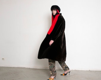 Può includere: Una persona indossa un lungo cappotto in finta pelliccia marrone scuro con una sciarpa rosso vivo e un cappello di pelliccia nero. La persona indossa anche pantaloni mimetici e mules neri con tacco alto con dettagli arancioni e gialli.