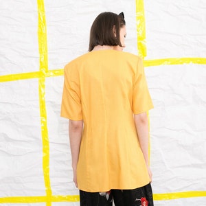May include: A yellow short-sleeved blouse with a V-neckline. The blouse is made of a lightweight fabric and has a relaxed fit.