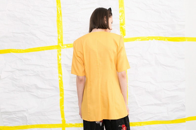 May include: A yellow short-sleeved blouse with a V-neckline. The blouse is made of a lightweight fabric and has a relaxed fit.