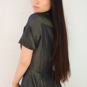 May include: A woman with long dark hair is wearing a dark green, textured, short-sleeved dress. She is looking over her shoulder.