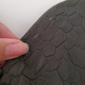 May include: Close-up of a dark green fabric with a textured pattern of small, raised circles.