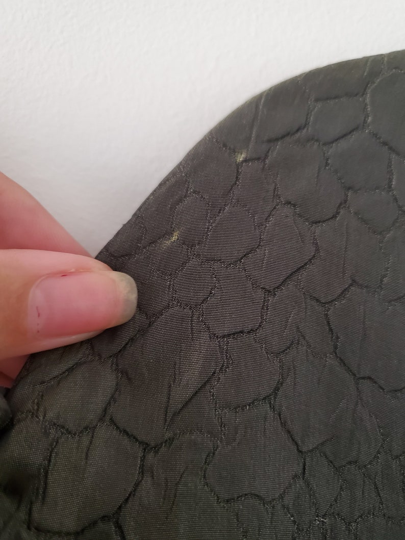 May include: Close-up of a dark green fabric with a textured pattern of small, raised circles.