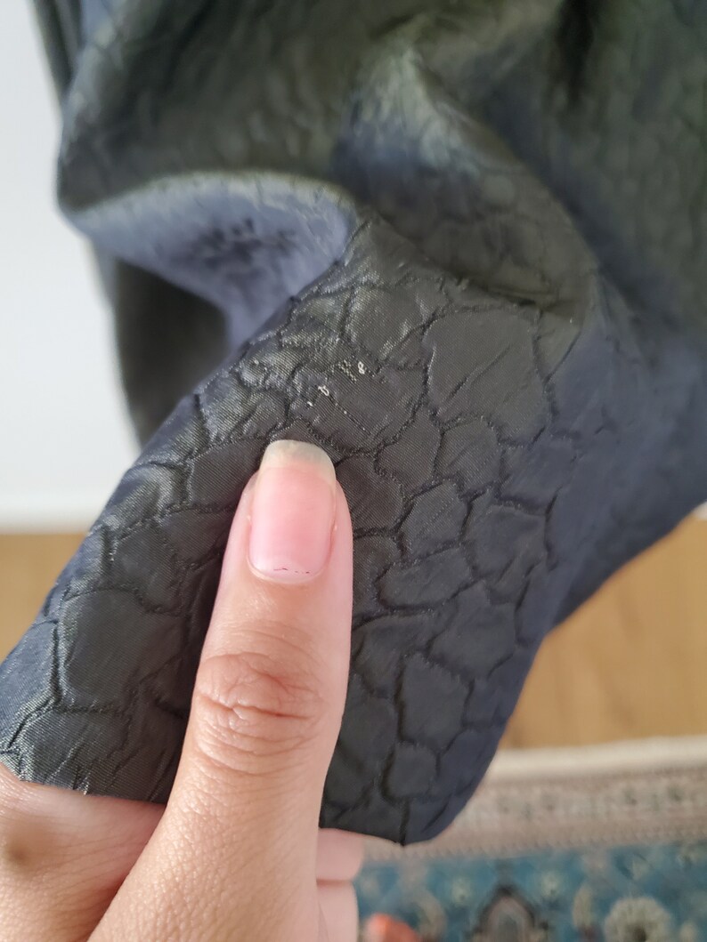 May include: Close-up of a dark green fabric with a textured, quilted pattern. The fabric is soft and has a subtle sheen.