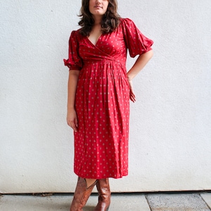 May include: A woman wearing a red midi dress with a white floral pattern and brown cowboy boots.
