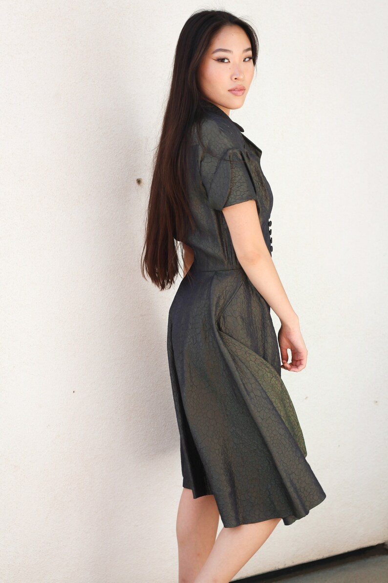 May include: A woman wearing a dark green, textured, short-sleeved dress with a button-up front.