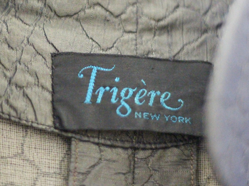 May include: A black label with the text "Trigere New York" in blue cursive lettering.