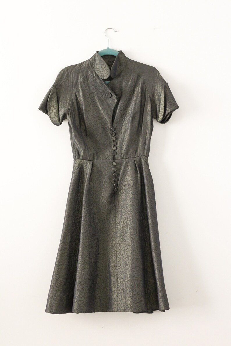 May include: A gold metallic dress with a button-up front and short sleeves. The dress has a fitted bodice and a full skirt.