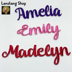May include: Three embroidered iron-on patches with the names Amelia in purple, Emily in pink, and Madelyn in red.