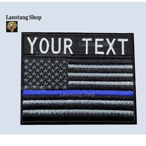 May include: Black and white embroidered American flag patch with a blue stripe across the middle. The patch has the text "YOUR TEXT" at the top.