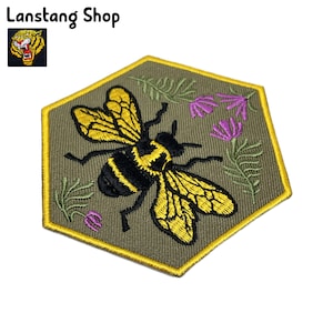 May include: A hexagonal embroidered patch with a yellow and black bee, green leaves, and purple flowers. The patch has a yellow border.