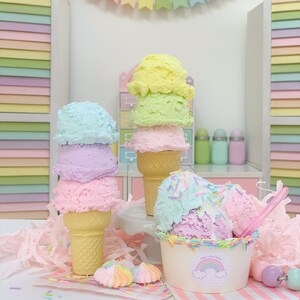 May include: Three pastel-colored ice cream cones with sprinkles and a bowl of ice cream with sprinkles. The ice cream is in a white bowl with a rainbow and the words "Kids Love Treats" on it. The ice cream is on a pink and white striped surface with a pink and white striped background.