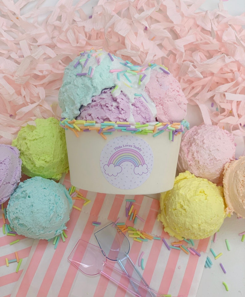 May include: A white ice cream cup with a rainbow sticker that says "Tilda Loves Teddy" and pastel-colored ice cream scoops. The ice cream is surrounded by pastel-colored sprinkles.
