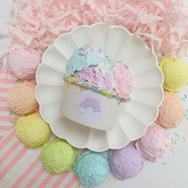 May include: A white paper cup filled with three scoops of pastel-colored ice cream. The ice cream is topped with colorful sprinkles and a sticker that says "This Love is Truly" with a rainbow graphic. The cup is surrounded by pastel-colored ice cream scoops on a white plate.