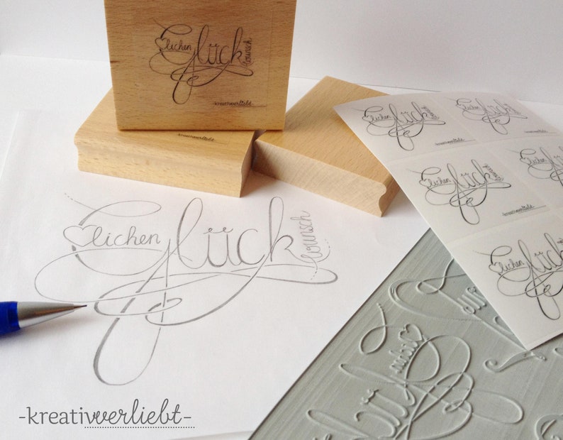 May include: A set of wooden stamps with the word "Gl&uuml;ckwunsch" (German for congratulations) in a cursive script. The stamps are used to create custom greeting cards and other paper crafts.