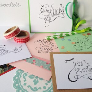 May include: Five different cards with handwritten calligraphy on them. The cards are on a white surface with colorful washi tape and a green straw. The cards say "Frohe Weihnachten", "Alles Gute", "Happy Birthday", "Just Married", and "Lieben Gl&uuml;ckwunsch".