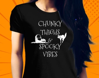 May include: A black short-sleeved t-shirt featuring white text that reads CHUNKY THIGHS & SPOOKY VIBES. The design includes a graphic of a tombstone marked R.I.P., a jack-o'-lantern, and a silhouette of an arched-back cat with its fur standing up.