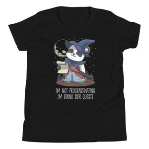 May include: Black t-shirt featuring a cartoon panda dressed as a wizard, holding a scroll and wand. The panda is set against a night sky with a moon and stars. Text reads: "I'M NOT PROCRASTINATING I'M DOING SIDE QUESTS."