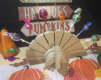 May include: A wooden turkey-shaped stand with a fan-shaped tail holds a variety of colorful lollipops. The stand is decorated with fall-themed signs that read "Sunflowers", "Hayrides", and "Pumpkins".