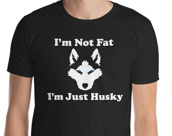 May include: Black t-shirt with the text "I'm Not Fat I'm Just Husky" in white, along with a white husky dog face graphic. The shirt is short-sleeved and made of a soft material.