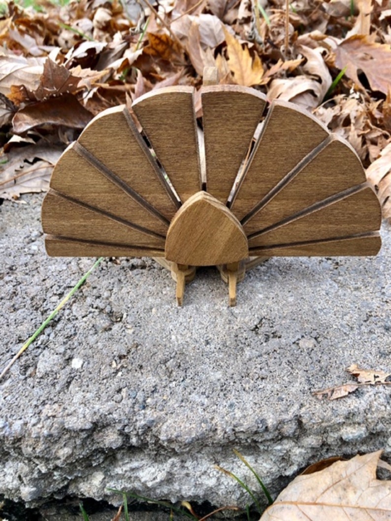 Op de afbeelding: Houten kalkoenfiguur met een bruine afwerking en een waaiervormige staart. Het figuur staat op een grijs betonnen oppervlak.
