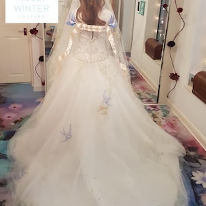 May include: A white wedding dress with a long train and a veil. The dress has a sweetheart neckline and is decorated with delicate embroidery and beading. The veil is trimmed with lace and has a satin ribbon.