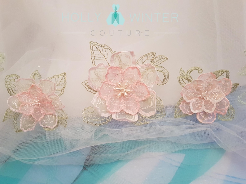May include: Three delicate pink and gold floral appliques with pearl accents on a white tulle background. The appliques are perfect for adding a touch of elegance to any project.