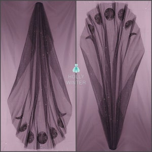 May include: A black tulle wedding veil with a sparkly finish and a design of moons in various phases. The veil is shown folded in half, with the design visible on both sides.