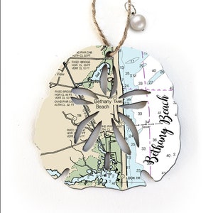 May include: White wooden ornament shaped like a seashell with a cutout design of a starfish. The ornament features a nautical chart of Bethany Beach, Delaware with the text "Bethany Beach" written in cursive.