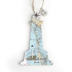 May include: A wooden lighthouse ornament with a nautical chart design and a compass charm. The ornament features the text "Boca Grande, Florida".
