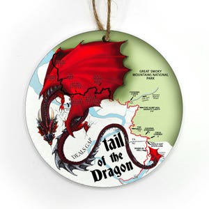 May include: Round wooden ornament featuring a red dragon with outstretched wings over a map of the Tail of the Dragon road in the Great Smoky Mountains National Park. The ornament has a string for hanging.
