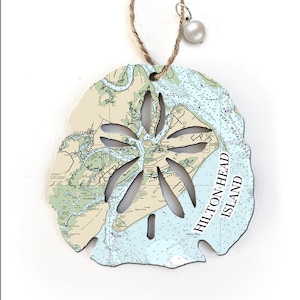 May include: A white and blue nautical map of Hilton Head Island, South Carolina, is printed on a sand dollar-shaped ornament. The sand dollar is cut out in the center, revealing the map underneath.