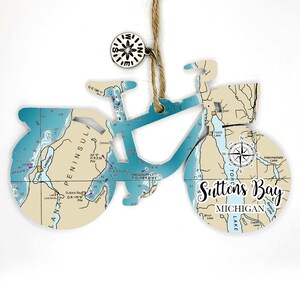 May include: A blue and white bicycle ornament with a nautical map design. The ornament features a compass and the text "Suttons Bay, Michigan".
