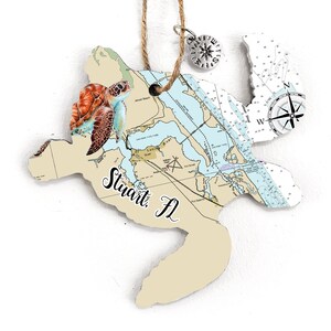 May include: A wooden sea turtle ornament with a nautical map design featuring the area around Stuart, Florida. The ornament includes a compass and the text "Stuart, FL".