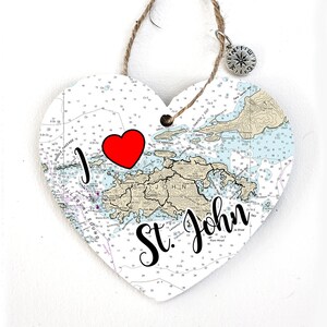 May include: A white heart-shaped ornament with a nautical chart of St. John, US Virgin Islands. The ornament has a red heart with "I love" written above it and "St. John" written in cursive below the chart.