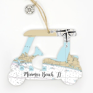 May include: A wooden golf cart ornament with a nautical map design and the text "Miramar Beach, FL". The ornament has a compass on top and a string for hanging.