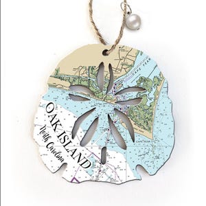 May include: A white sand dollar ornament with a nautical map of Oak Island, North Carolina. The ornament is made of wood and has a string for hanging.