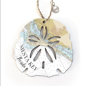May include: A white wooden sand dollar ornament with a nautical chart design and the text "SIESTA KEY Florida" on the front. The ornament has a string loop for hanging.