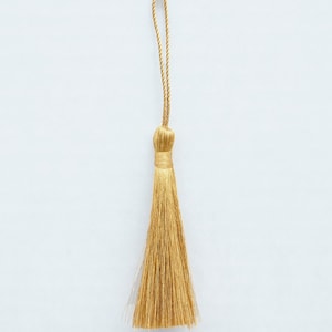 May include: A gold tassel with a long, thin cord. The tassel is made of soft, fine fibers and has a delicate, elegant appearance.