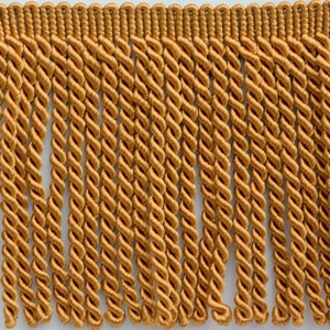 May include: Gold fringe trim with a twisted cord design. The fringe is approximately 1 inch in length.