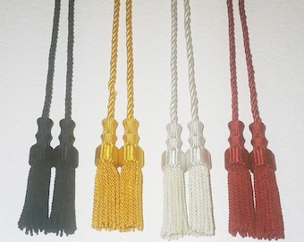 May include: Four graduation tassel cords with double tassels. The cords are black, gold, white, and red.