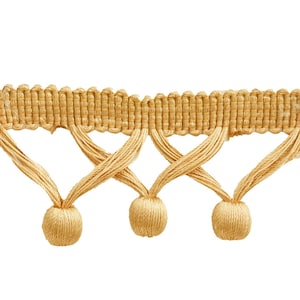 Peut inclure: Gros plan d'une garniture décorative beige clair. La garniture présente une section supérieure tissée et une série de pompons noués suspendus. Les pompons sont espacés de manière uniforme, créant un motif attrayant.