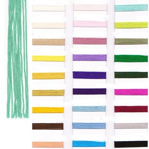 Puede incluir: Una carta de colores con varios tonos de cinta y cordón. La carta muestra una gama de colores, incluyendo blanco, rojo, rosa, morado, azul, verde y negro. Un manojo de cordón verde menta está a la izquierda.